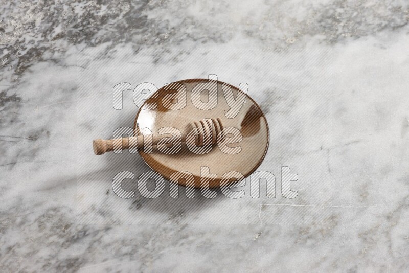 Multicolored pottery plate with wooden honey dipper in it on grey marble background