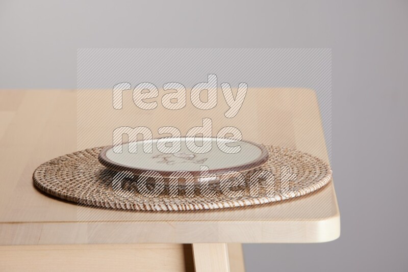 multi-colored pottery Plate placed on a big light colored straw placemat on the edge of wooden table