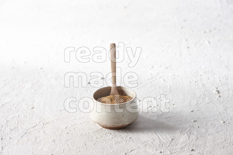 Ceramic beige bowl full of cinnamon powder with a wooden spoon on a textured white background