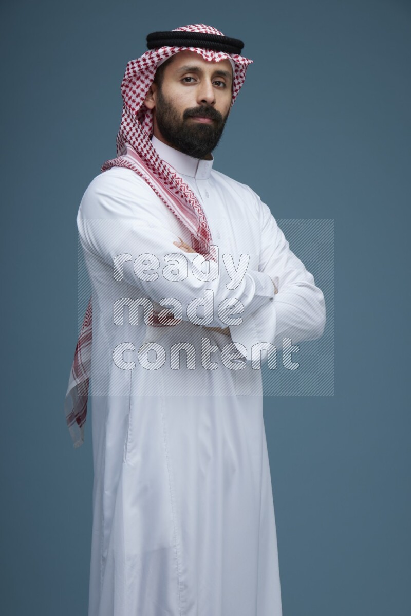 A man posing in a blue background wearing Saudi Thob and Shomag