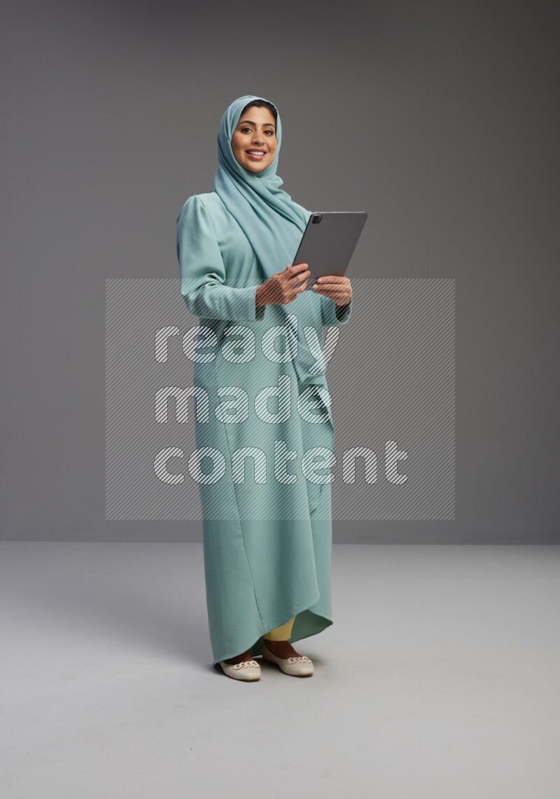Saudi Woman wearing Abaya standing working on tablet on Gray background