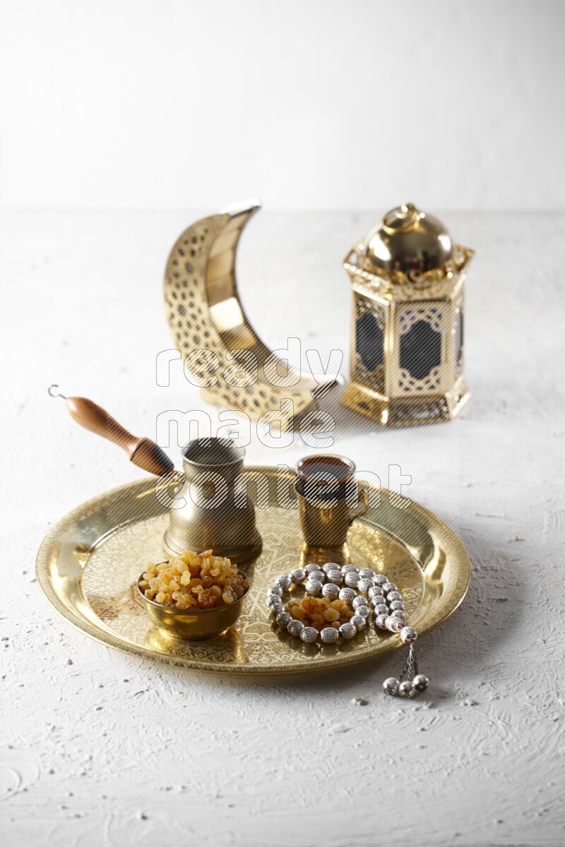 Raisins in a metal bowl with coffee and prayer beads on a tray beside lanterns in a light setup