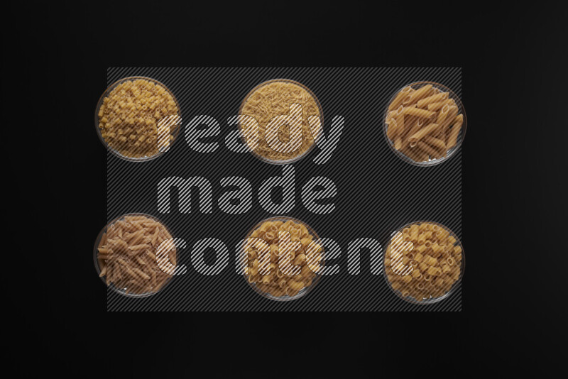 Different pasta types in 6 glass bowls on black background