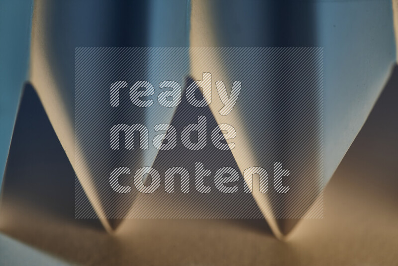 A close-up abstract image showing sharp geometric paper folds in blue gradients and warm tones