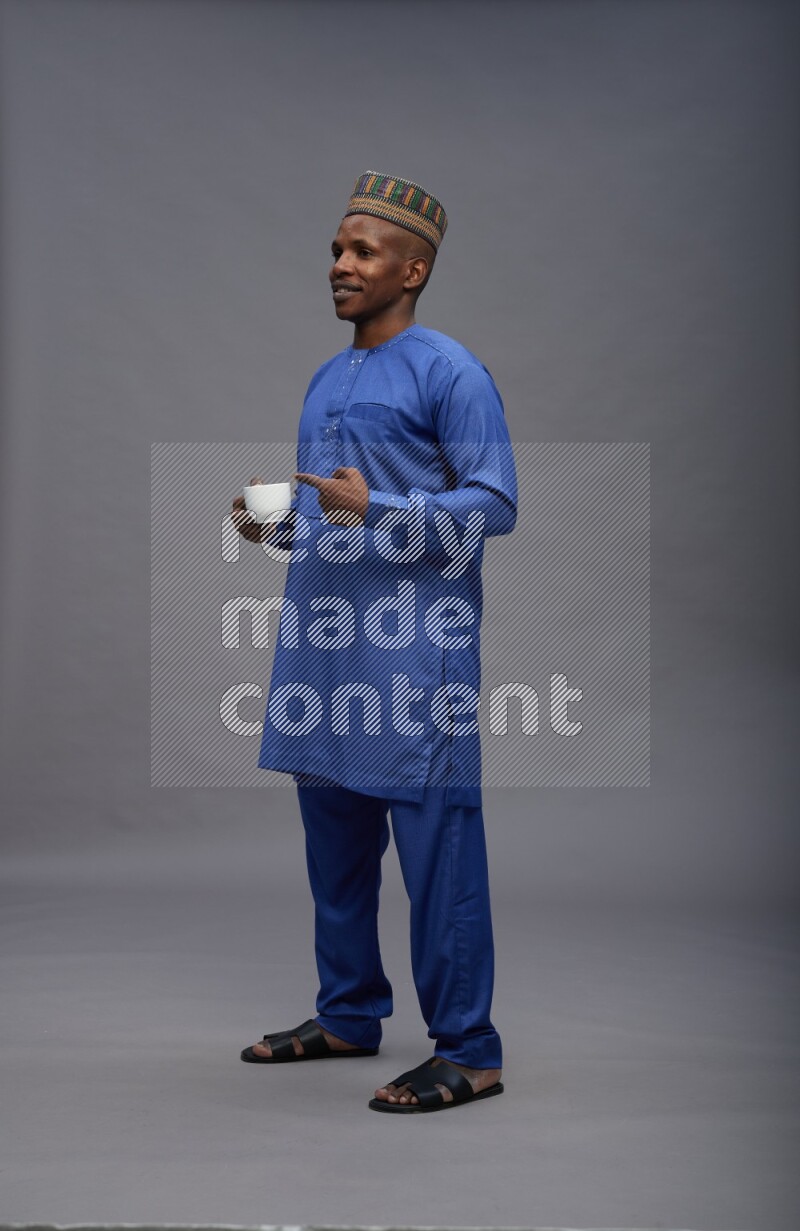 Man wearing Nigerian outfit standing holding mug on gray background
