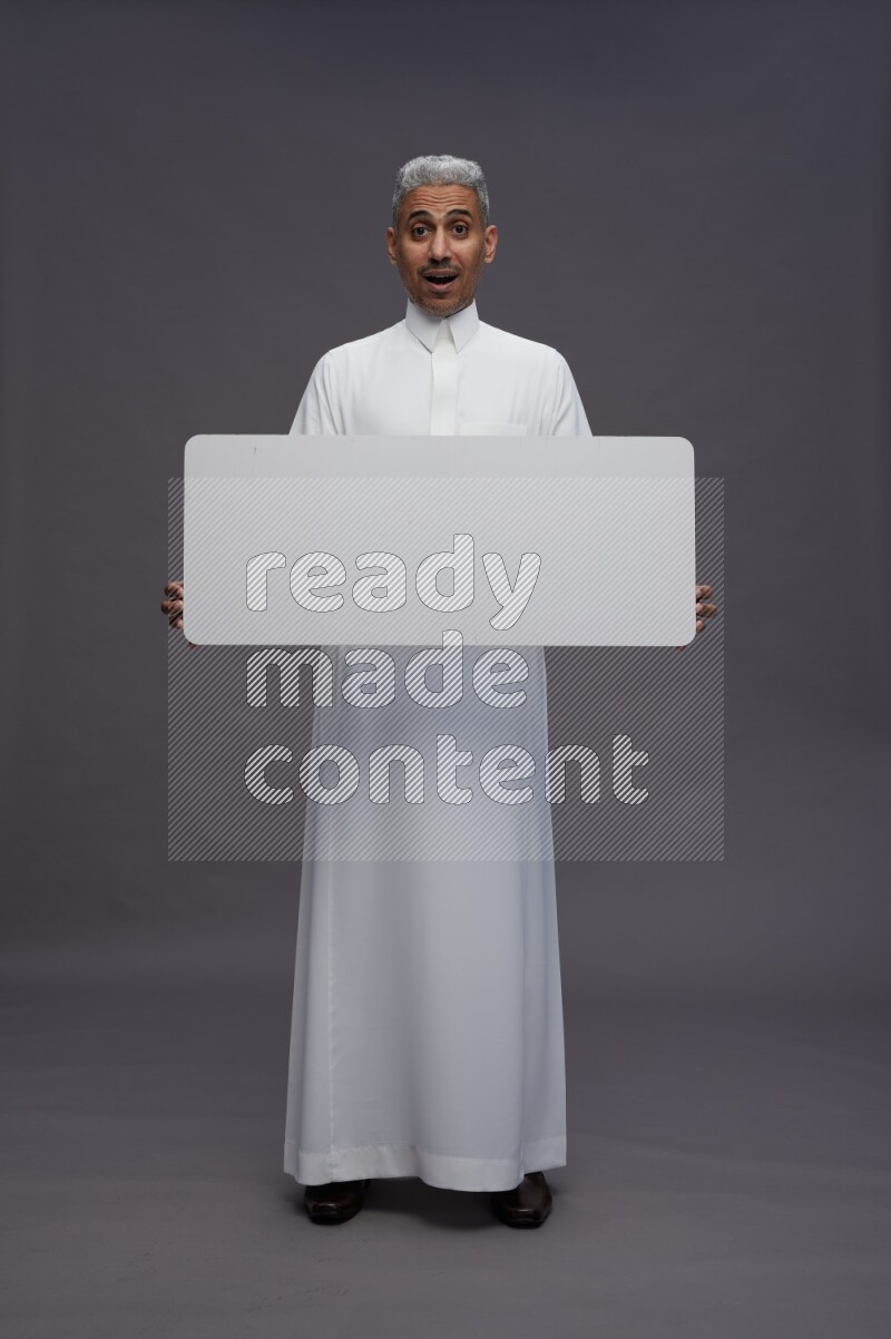 Saudi man wearing thob standing holding board on gray background