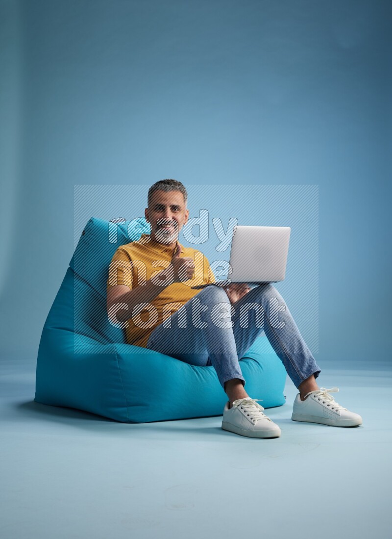 A man sitting on a blue beanbag and working on laptop