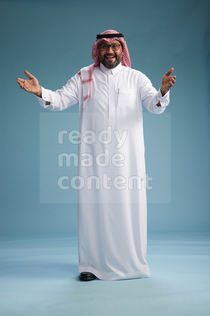 Saudi Man with shimag Standing Interacting with the camera on blue background