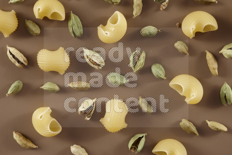 Raw pasta with different ingredients such as cherry tomatoes, garlic, onions, red chilis, black pepper, white pepper, bay laurel leaves, rosemary and cardamom on beige background