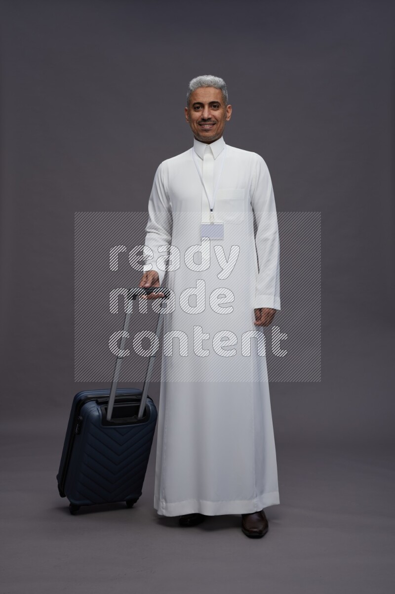 Saudi man wearing thob with neck strap employee badge standing holding bag on gray background