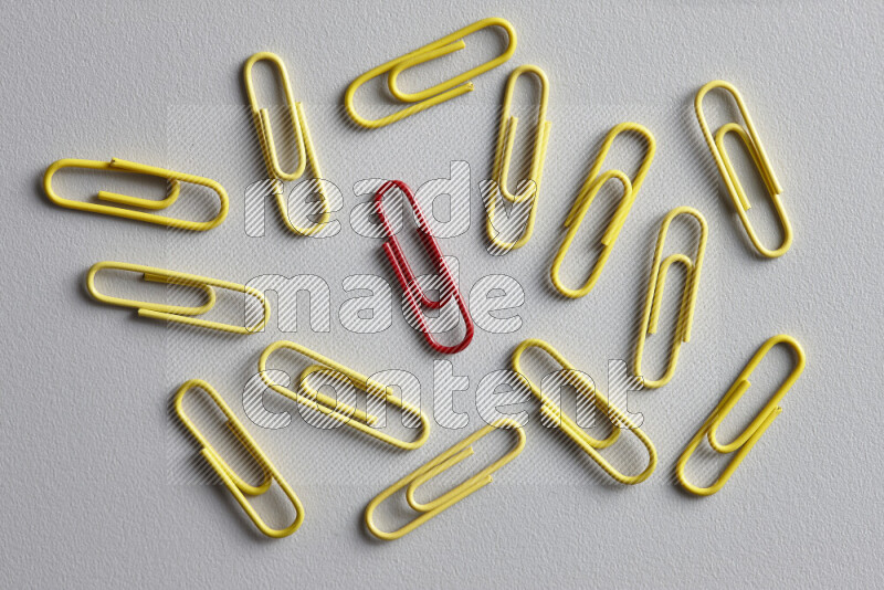 A bunch of yellow paper clips with a different colored paper clip in the center on grey background