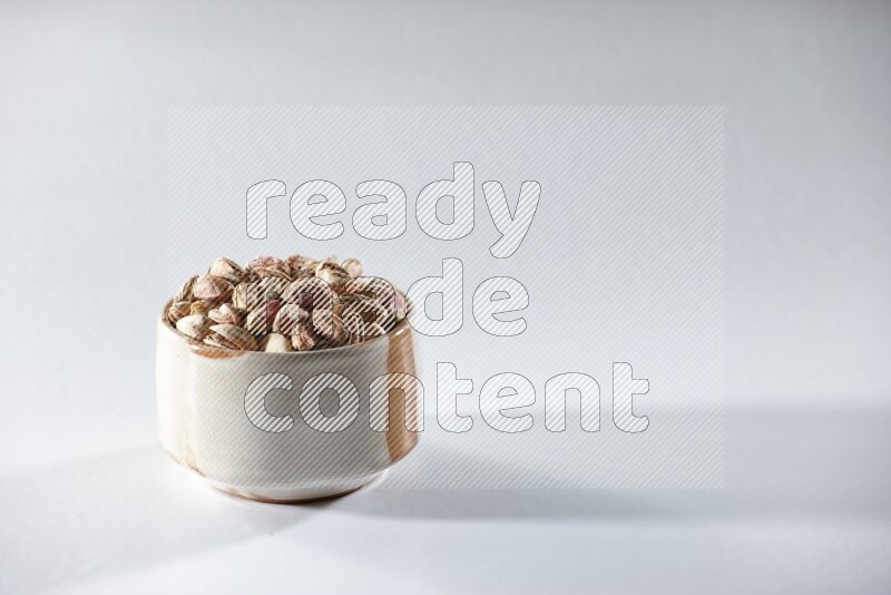 A beige ceramic bowl full of peeled pistachios on a white background in different angles
