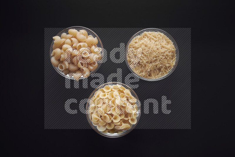 Different pasta types in glass bowls on black background
