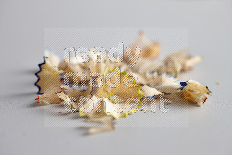 A close-up showing a small pile of pencil shavings with varied color edges on grey background