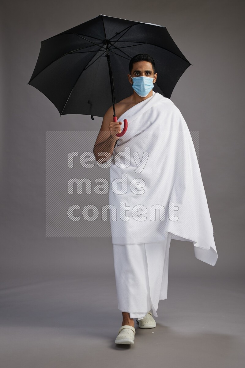 A man wearing Ehram and mask Standing holding umbrella on gray background on gray background