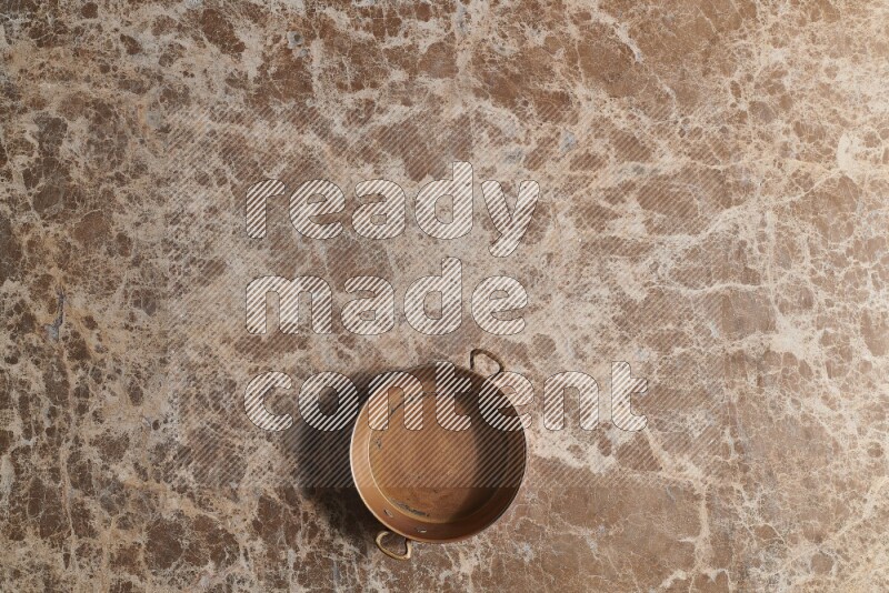 A small copper pan on beige marble background