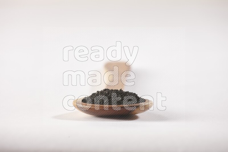 A wooden ladle full of black seeds on a white flooring