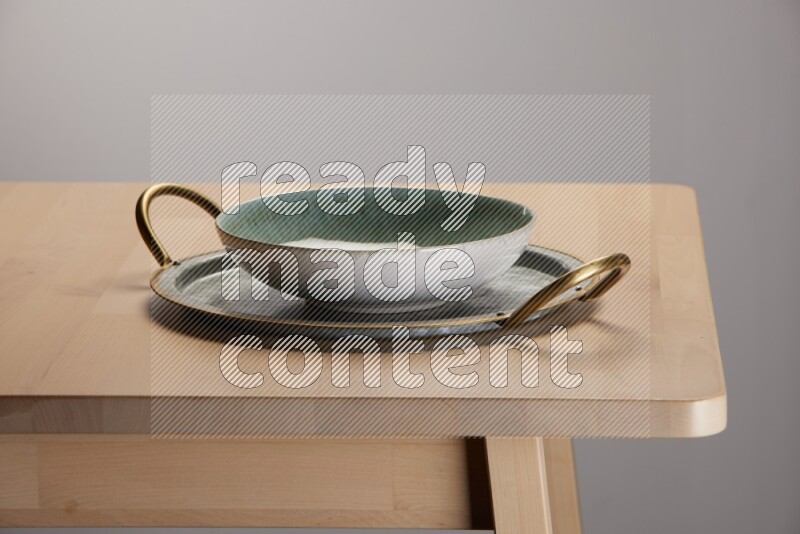 multicolored bowl placed on a rounded stainless steel tray with golden handels on the edge of wooden table