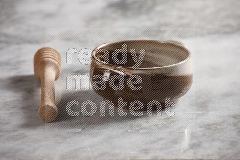 Multicolored pottery bowl with wooden honey dipper on the side on grey marble background