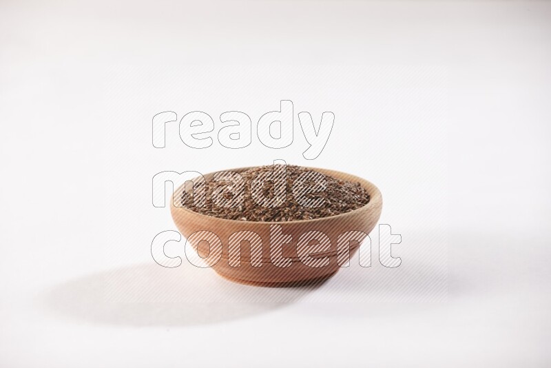 A wooden bowl full of flax seeds on a white flooring
