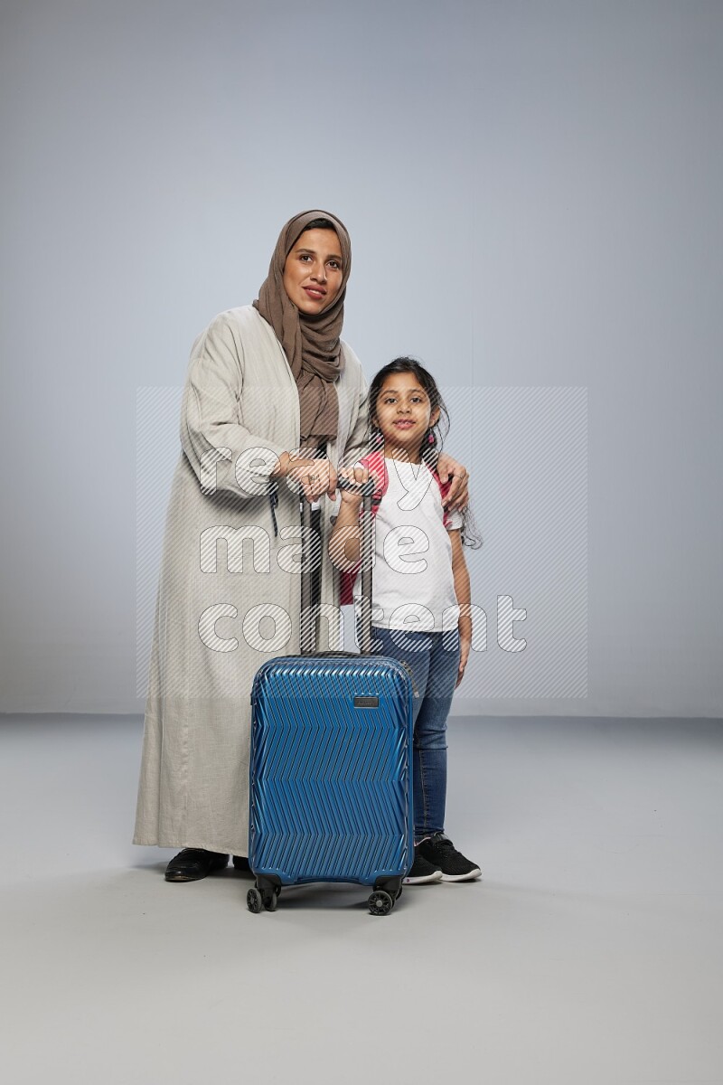 Mom and daughter standing pulling a carry-on bag on gray background