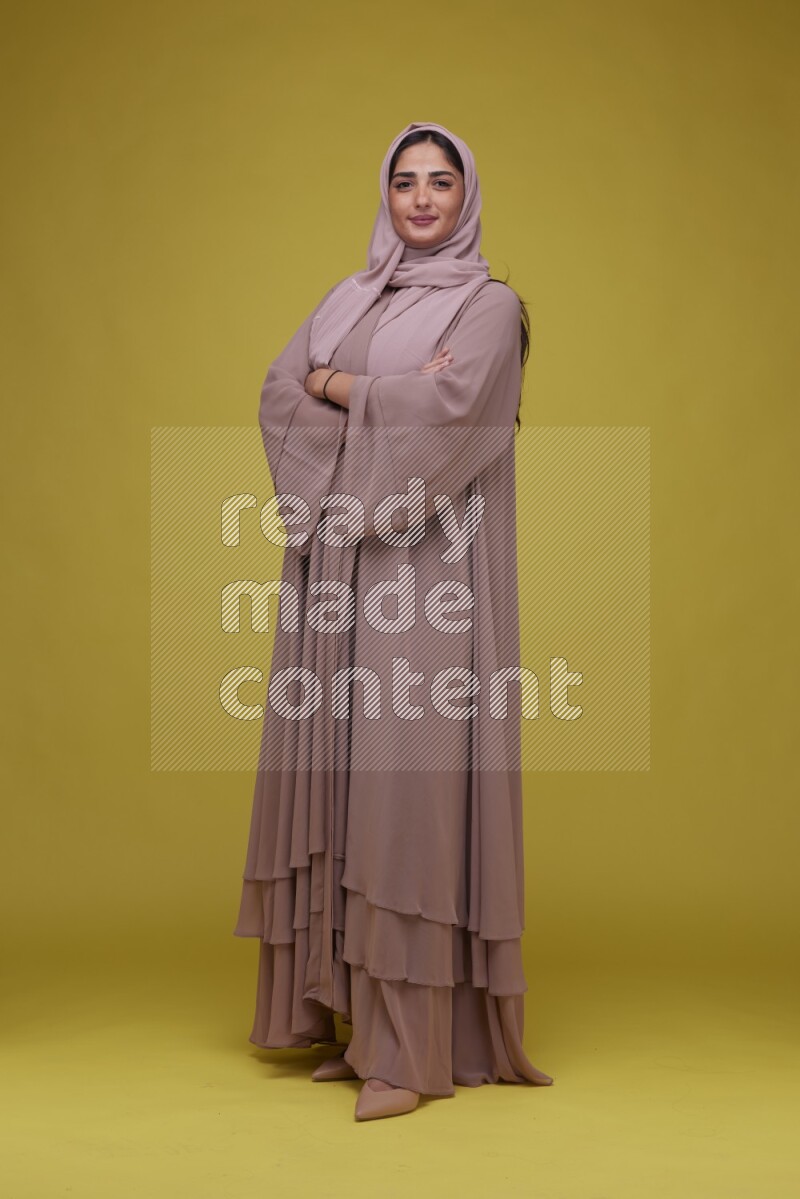 A woman Posing on a Yellow Background wearing Brown Abaya with Hijab
