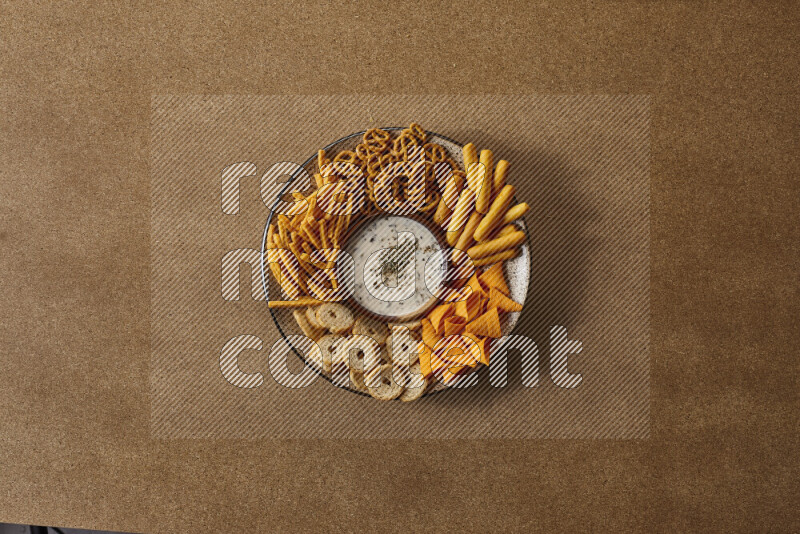 Assorted snacks on a pottery plate with a dipping on brown background
