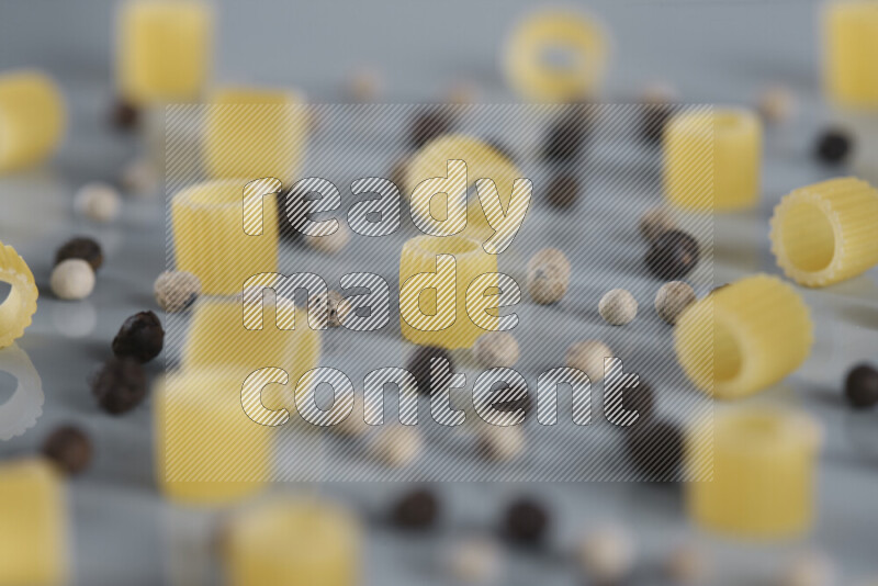 Raw pasta with different ingredients such as cherry tomatoes, garlic, onions, red chilis, black pepper, white pepper, bay laurel leaves, rosemary, cardamom and mushrooms on light blue background