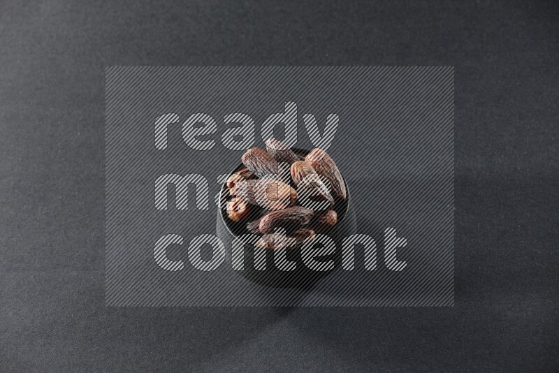 A black pottery bowl full of dried dates on a black background in different angles