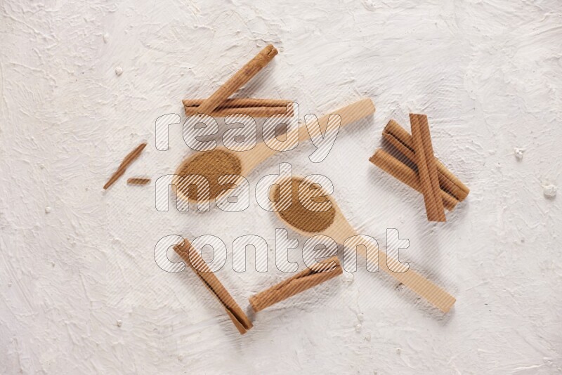 Two wooden spoons full of cinnamon powder with cinnamon sticks on white background