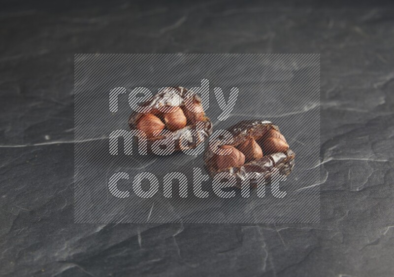 two hazelnuts stuffed madjoul dates on a black textured background