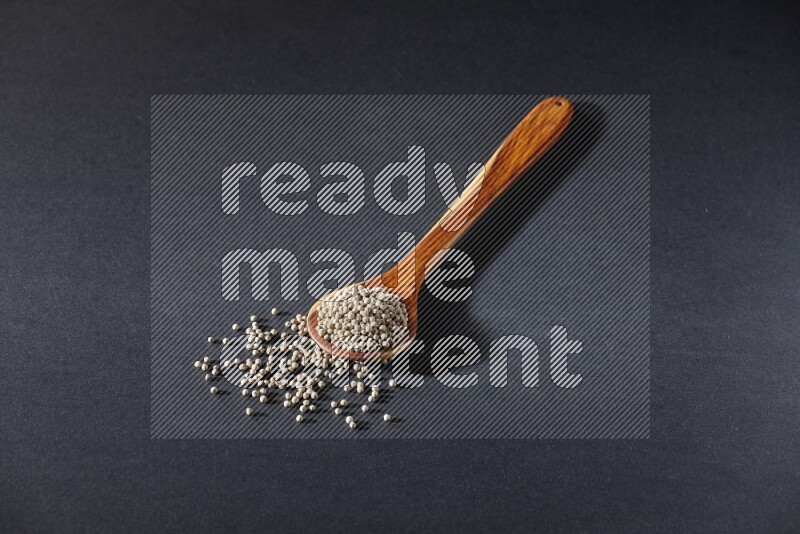 A wooden ladle full of white pepper beads on black flooring