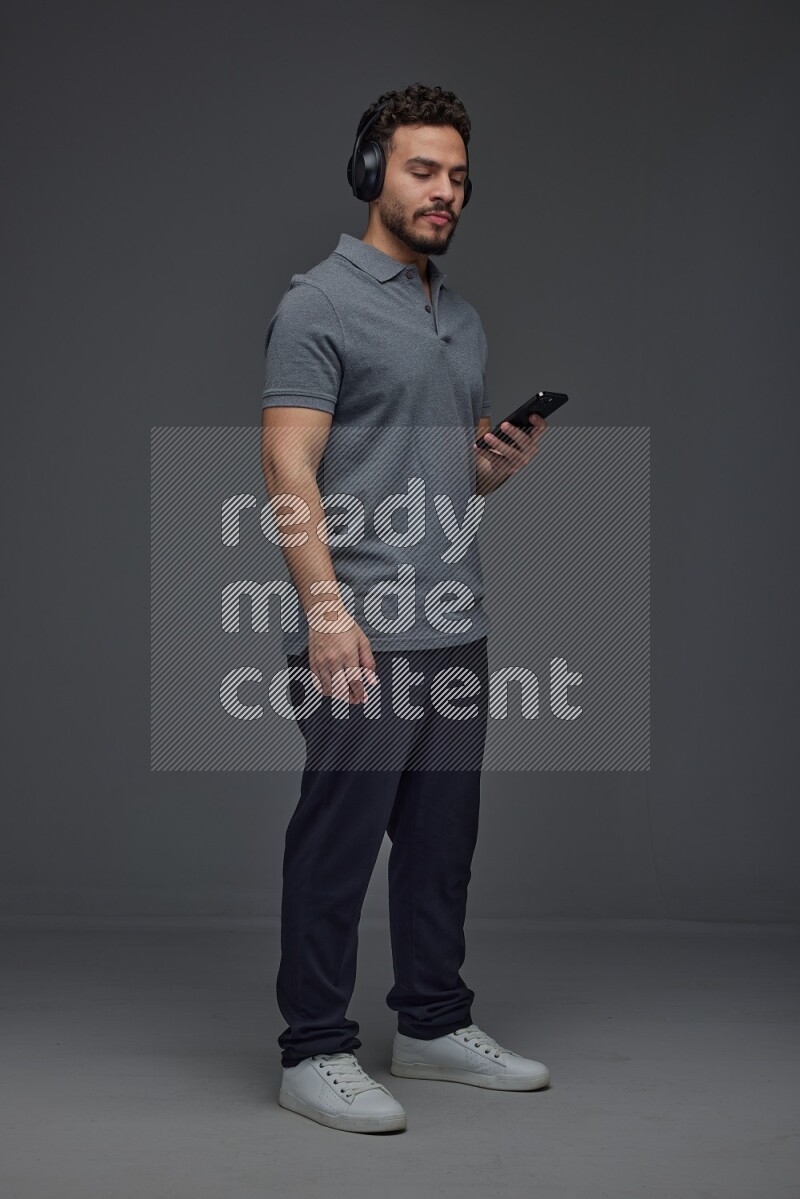 A man wearing casual and using his phone and headphone eye level on a gray background