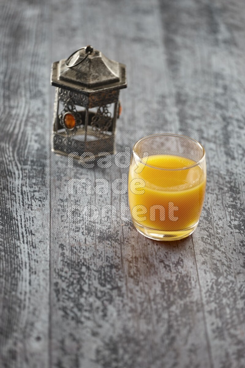 A silver lantern with different drinks, dates, nuts, prayer beads and quran on grey wooden background
