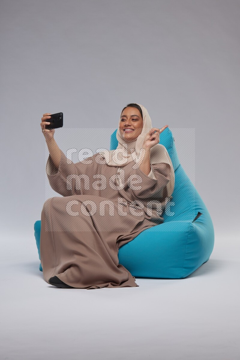 A Saudi woman sitting on a blue beanbag and taking selfie