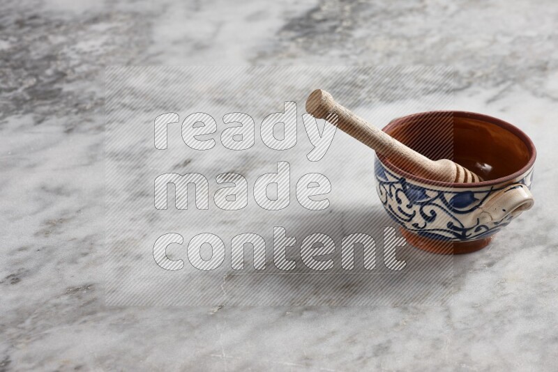 Decorative pottery pot with wooden honey dipper in it on grey marble background