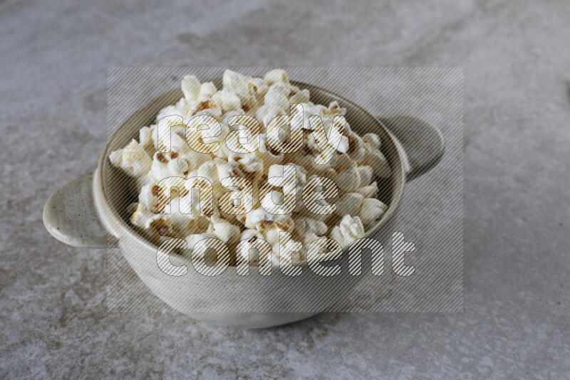 popcorn in a off-white handheld ceramic bowl on a grey textured countertop