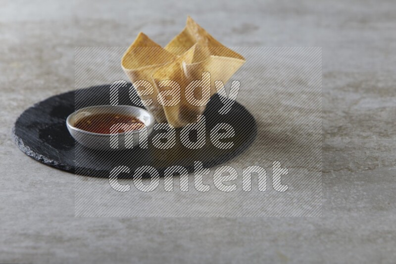 wonton cups with soy sauce ramkin on circle slate on grey textured counter top