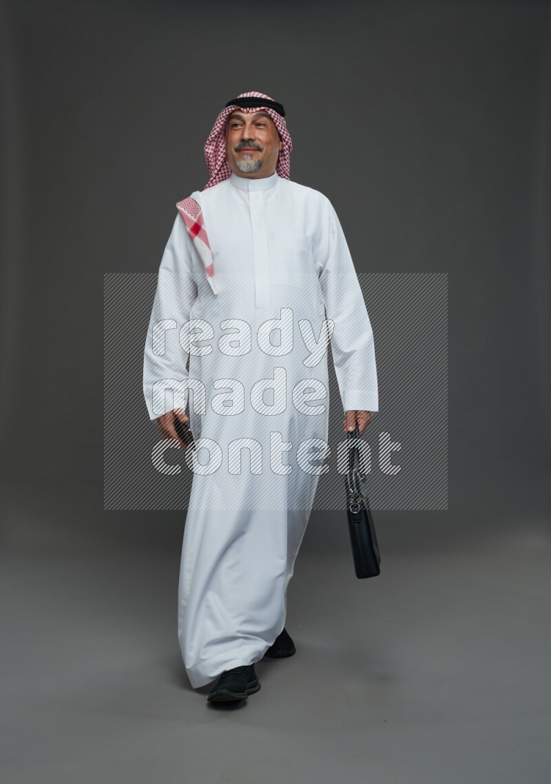 Saudi man with shomag Standing holding bag and phone on gray background