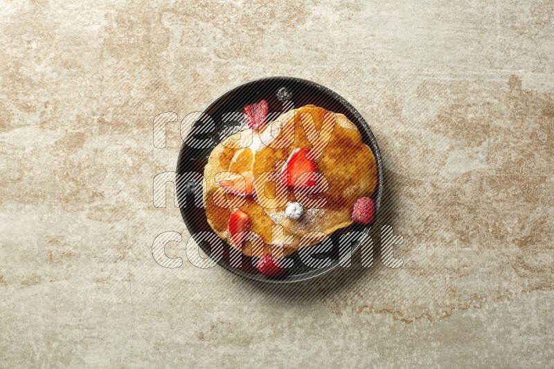 Three stacked mixed berries pancakes in a black plate on beige background