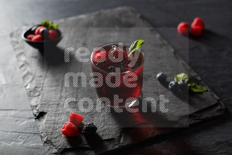 A glass of mixed berries juice with mint leaves on black background