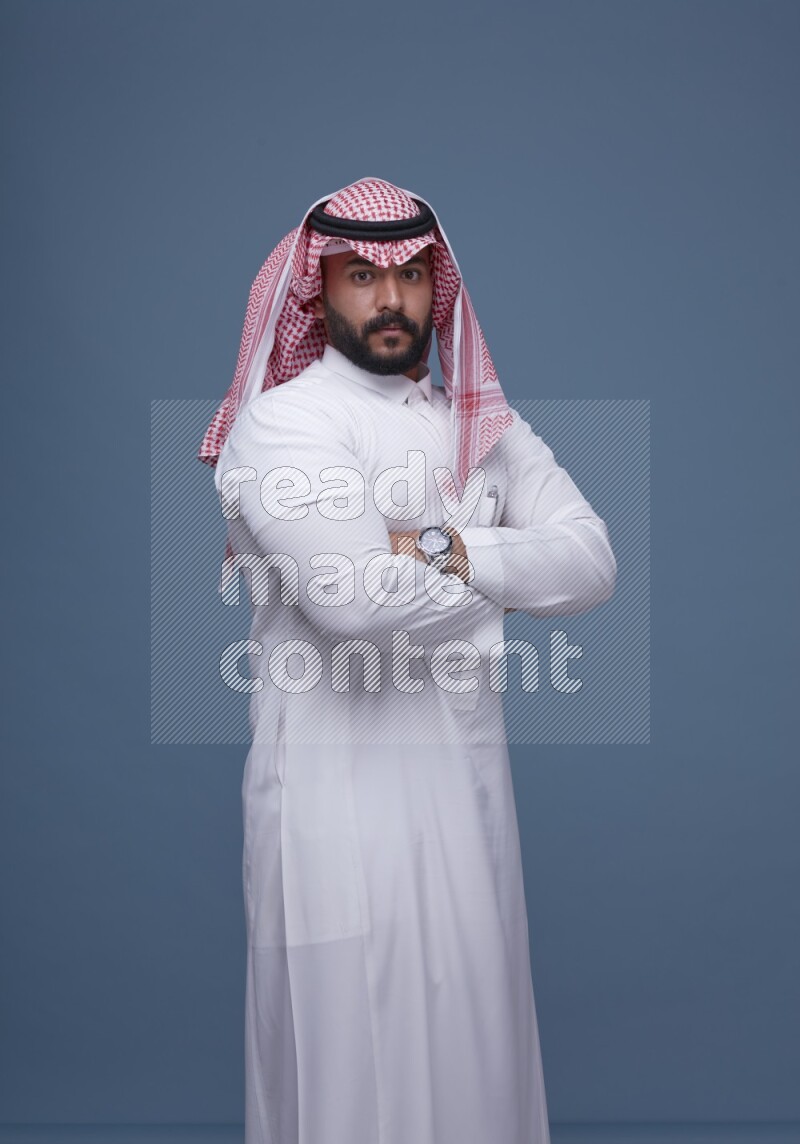 A Saudi man posing on blue background wearing Thob and Shomag
