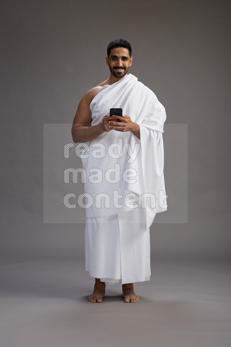 A man wearing Ehram Standing texting on phone on gray background
