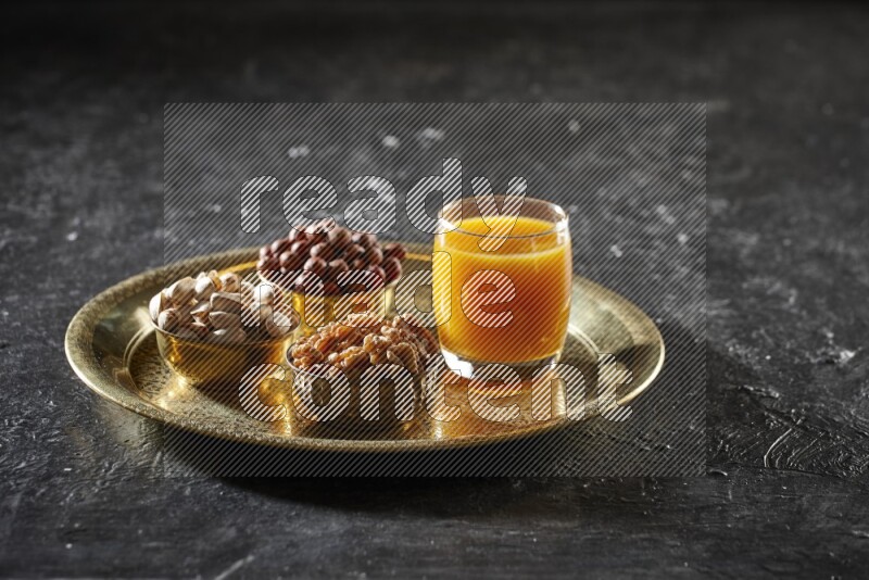 مكسرات في أطباق معدنية مع مشروب قمر الدين على صينية علي خلفية سوداء