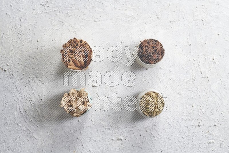 Cardamom, ginger, cinnamon sticks and star anise in 4 bowls on a textured white background