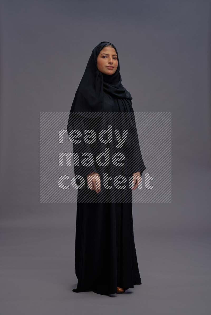 Saudi woman wearing Abaya standing interacting with the camera on gray background