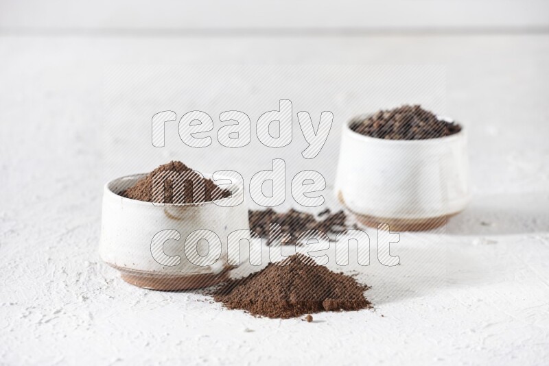 2 Beige ceramic bowls, one full of cloves and the other full of powder on textured white flooring