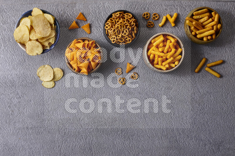 Assorted snacks in pottery bowls on grey background