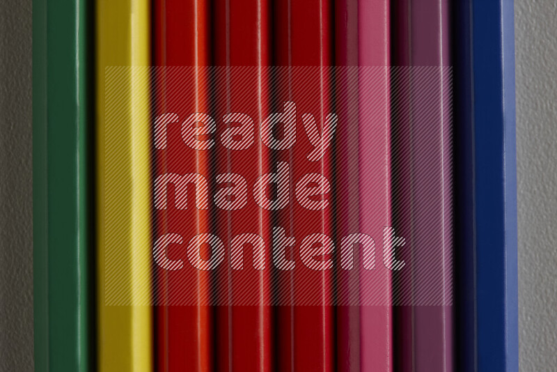 A collection of colored pencils arranged showcasing a gradient of different hues on grey background