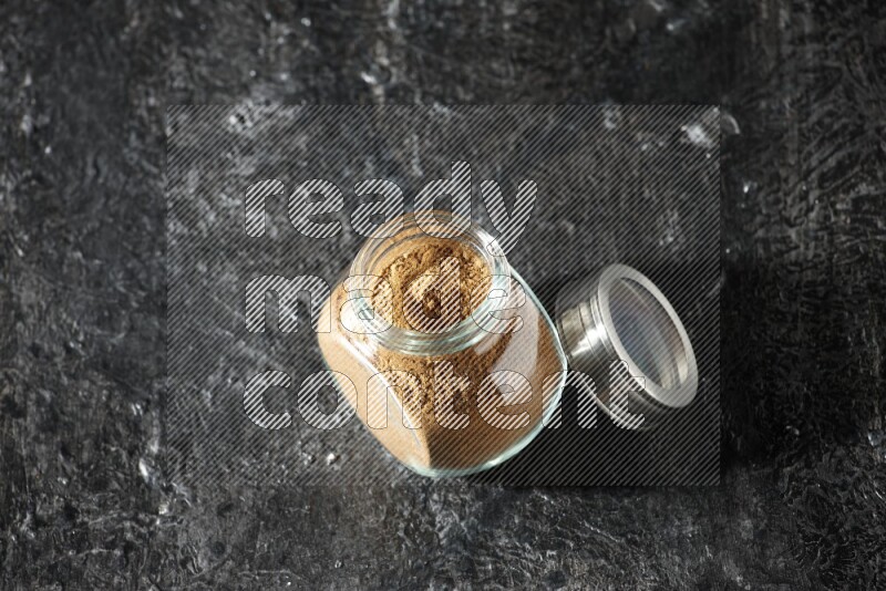 وعاء زجاجي للتوابل ممتلئ ببودرة بهار الفلفل الحلو على خلفية سوداء